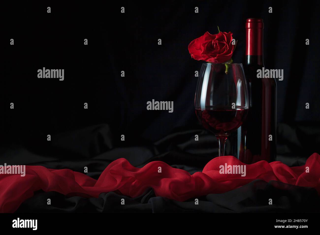Bouteille et verre de vin rouge avec rose rouge sur fond noir. Banque D'Images
