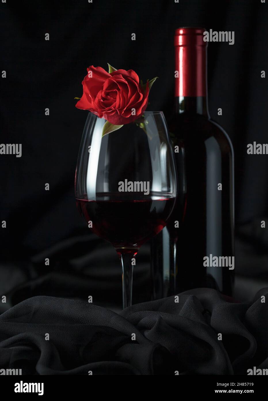 Bouteille et verre de vin rouge avec rose rouge sur fond noir. Banque D'Images