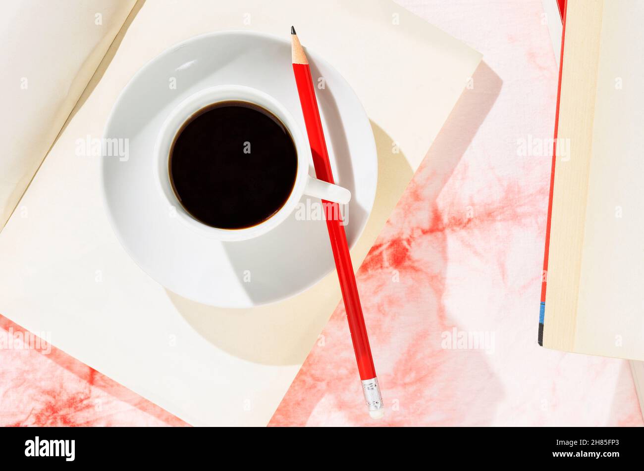 Tasse blanche de café avec crayon rouge sur livre ouvert, fond blanc et rouge Banque D'Images
