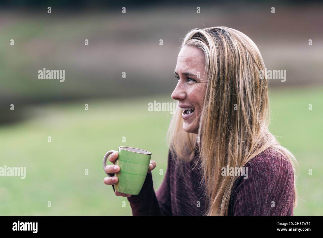 Femme blonde souriante qui boit du thé dans un parc Banque D'Images