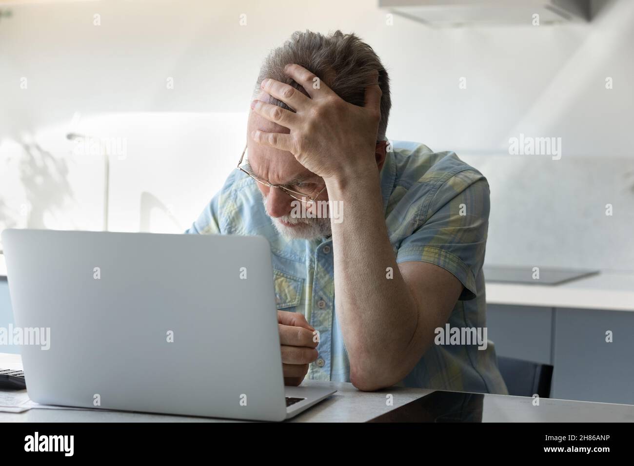 Un homme expérimenté frustré et fatigué se touchant la tête à un ordinateur portable Banque D'Images