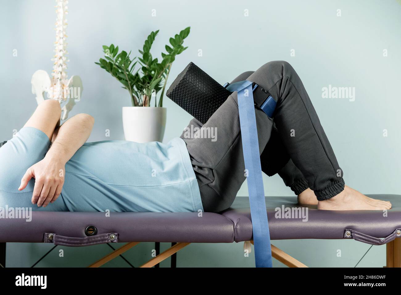 Un homme allongé sur la table de massage en position de repos constructive avec un rouleau en mousse et une ceinture de maligan Banque D'Images