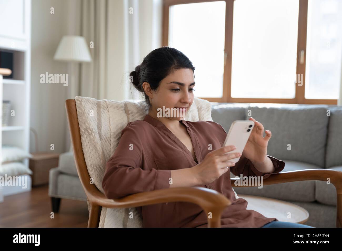 Jeune femme indienne décontractée utilisant un téléphone portable, assise dans un fauteuil. Banque D'Images