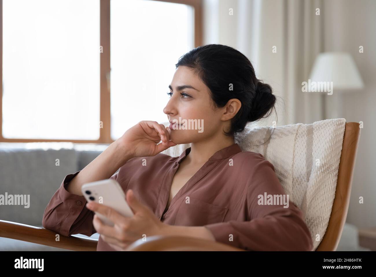 Bonne femme indienne rêveuse se reposant avec un téléphone portable dans les mains. Banque D'Images