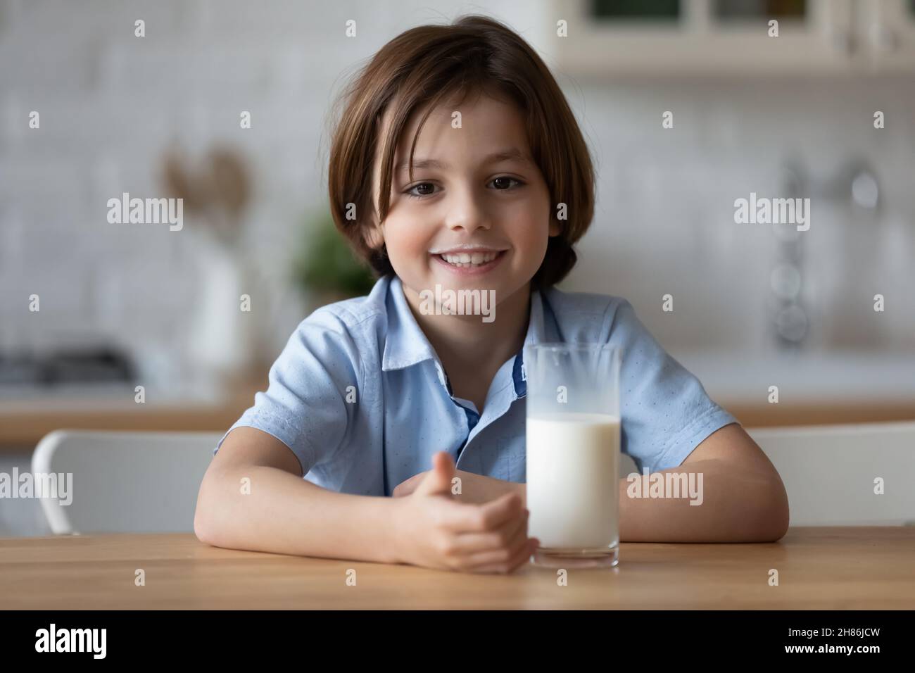 Un petit garçon mignon s'assoit à la table avec un verre de lait Banque D'Images