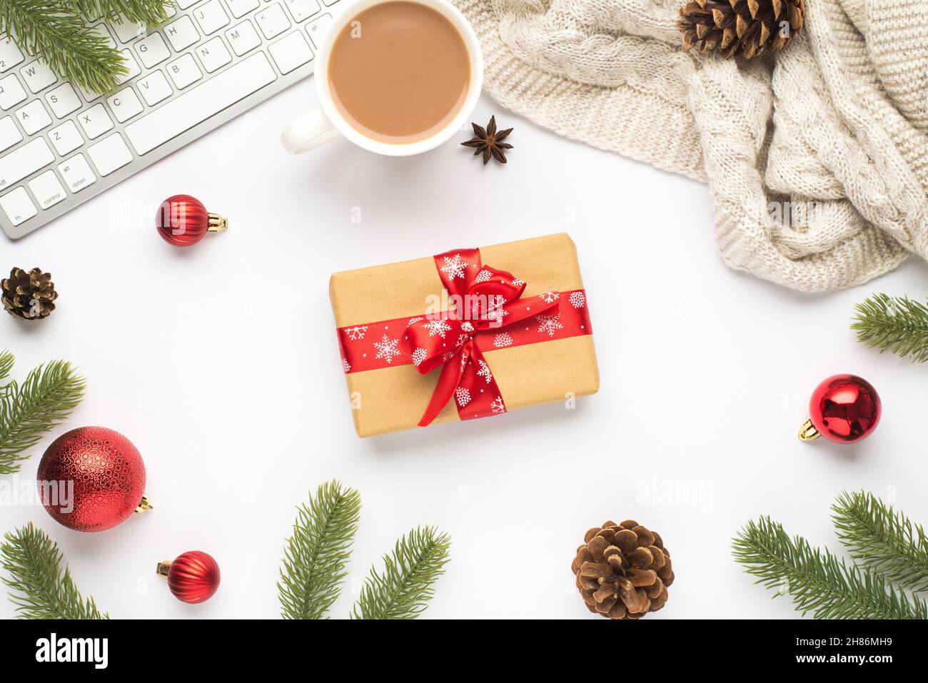 Vue du dessus photo du clavier tasse de hot buvant rouge arbre boules de noël brindilles pin rameaux cônes chandail anis et boîte-cadeau avec noeud rouge sur dos blanc isolé Banque D'Images