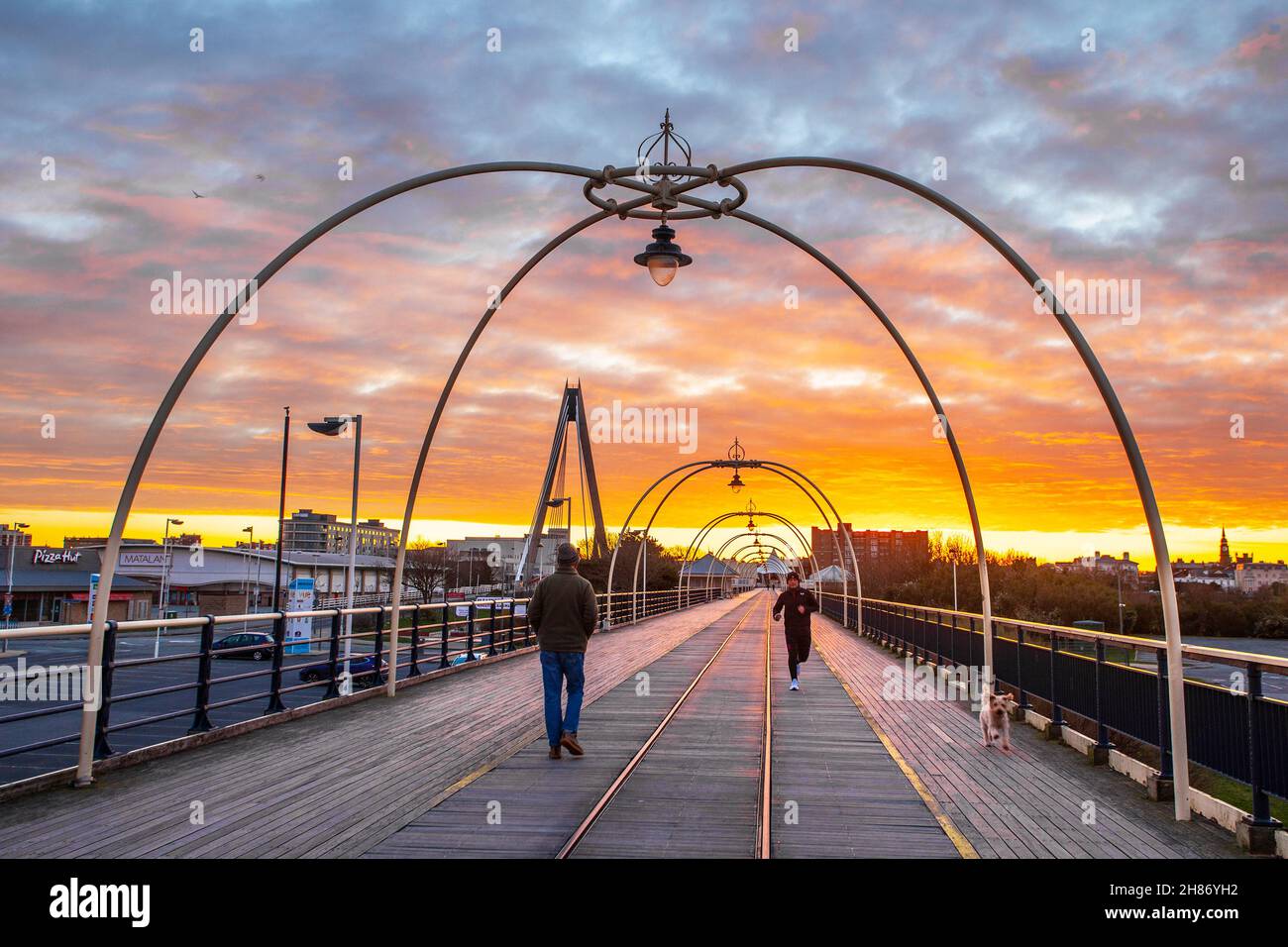 Southport, Merseyside.Météo Royaume-Uni.28 novembre 2021.Ciel rouge le matin -2C à l'aube tandis que les marcheurs de la jetée se promènent tôt le matin sur la jetée en fer victorienne du complexe.Aujourd'hui, les nuages vont s'y déplacer du nord et une petite pluie, de la neige et du luette se développeront.Une journée froide avec une douce brise du nord-ouest.Crédit; MediaWorldImages/AlamyLiveNews Banque D'Images