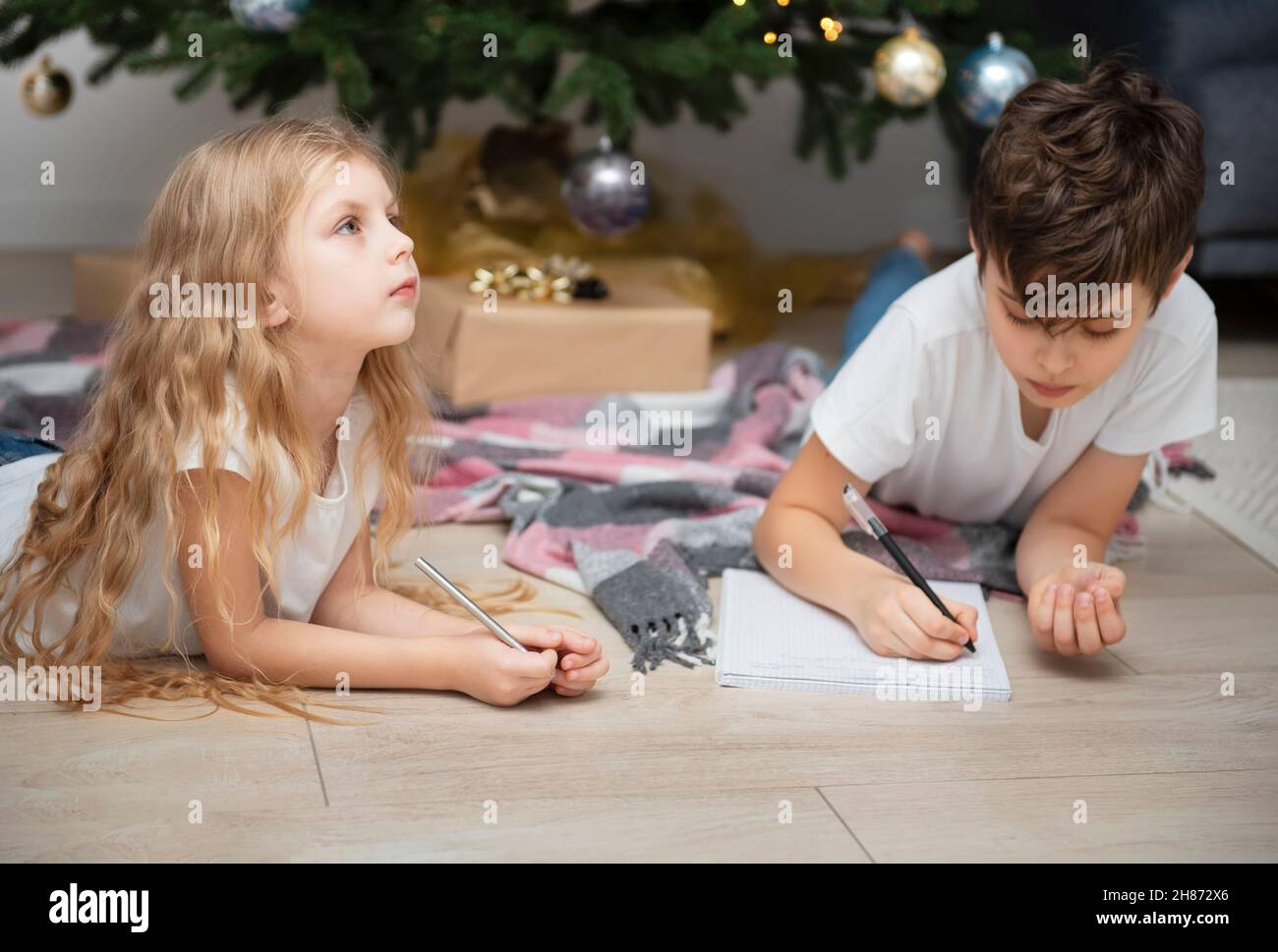 Enfants - un garçon et une fille écrivent des lettres au Père Noël près de l'arbre de Noël dans le salon Banque D'Images