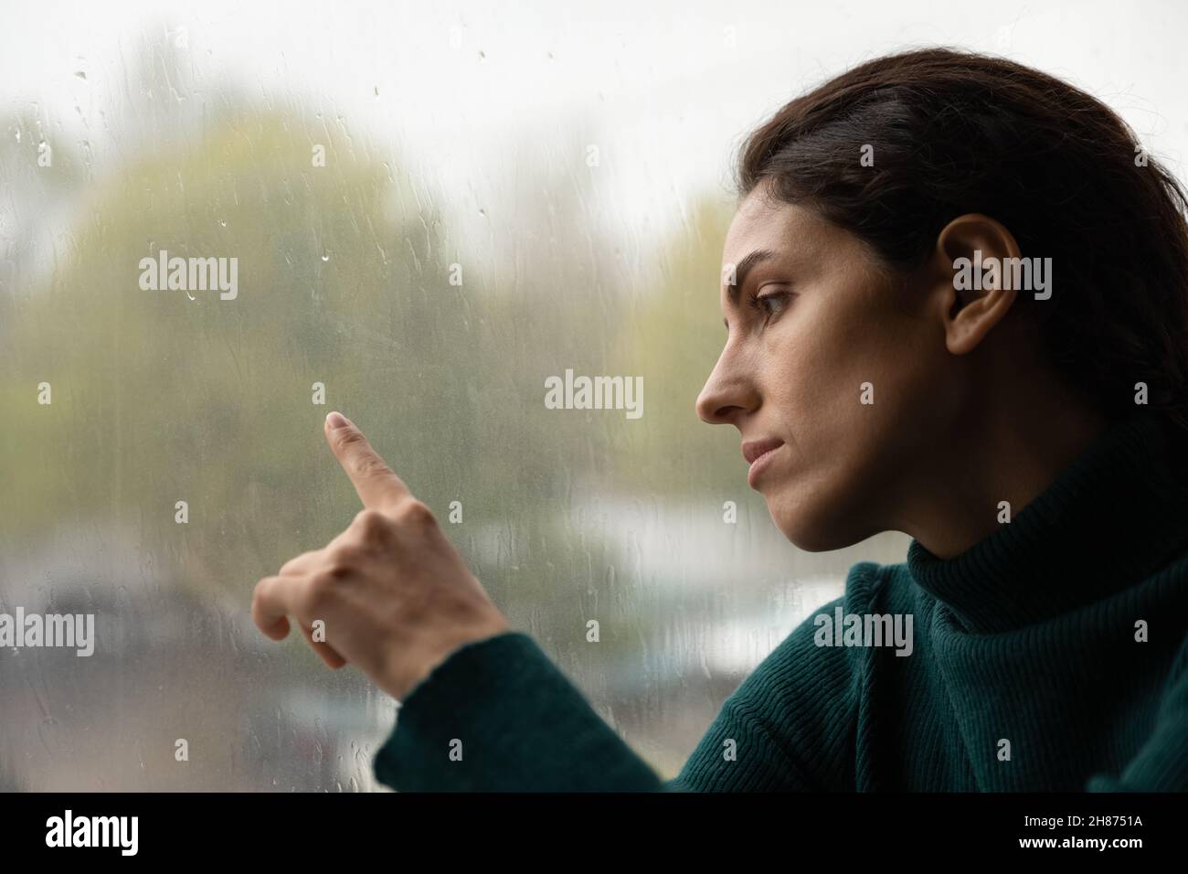 Triste femme millénaire assis par la fenêtre en train de courir le doigt sur le verre Banque D'Images