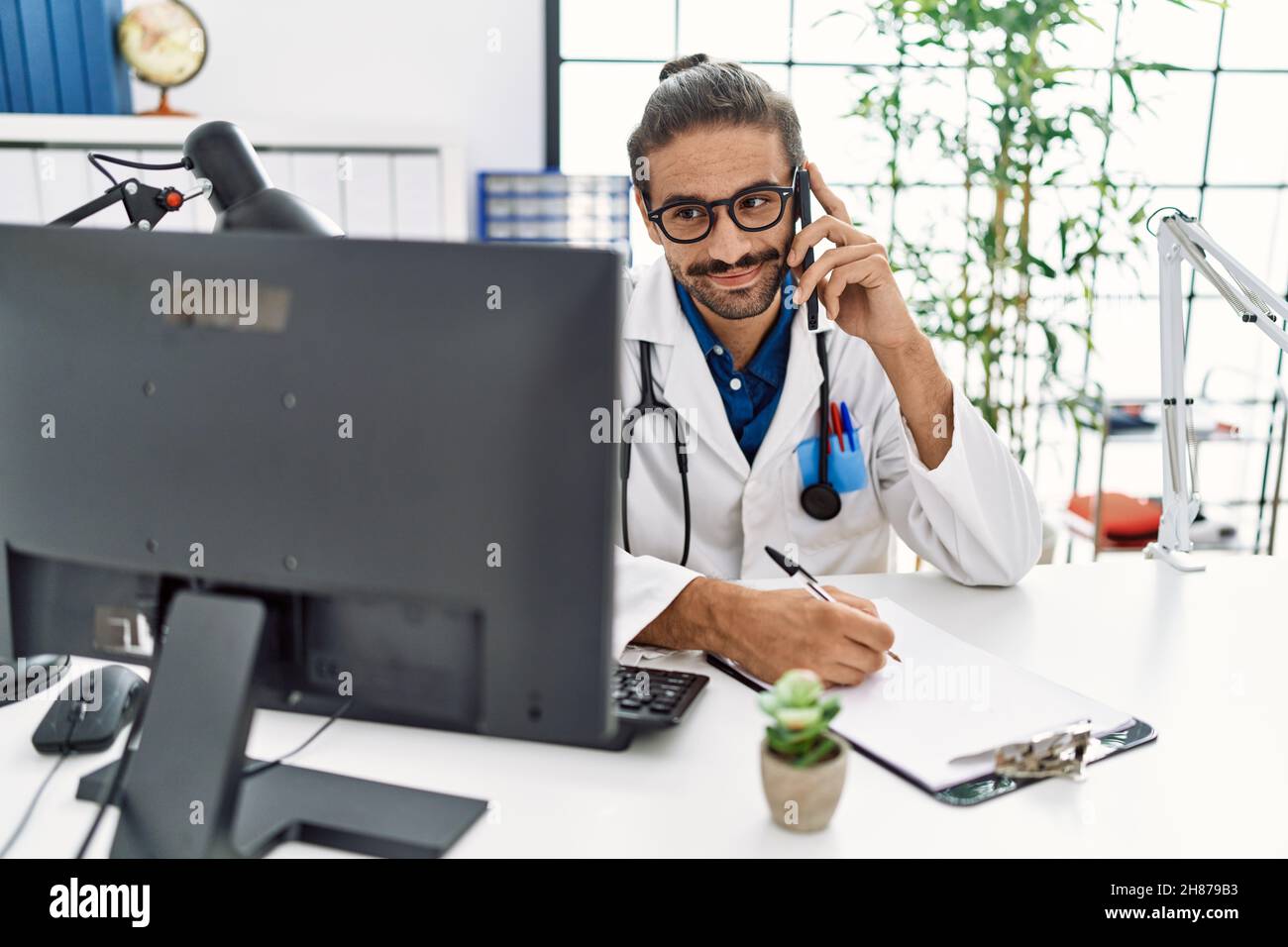 Beau hispanique homme écrivant la presciption au téléphone à la clinique de l'hôpital Banque D'Images