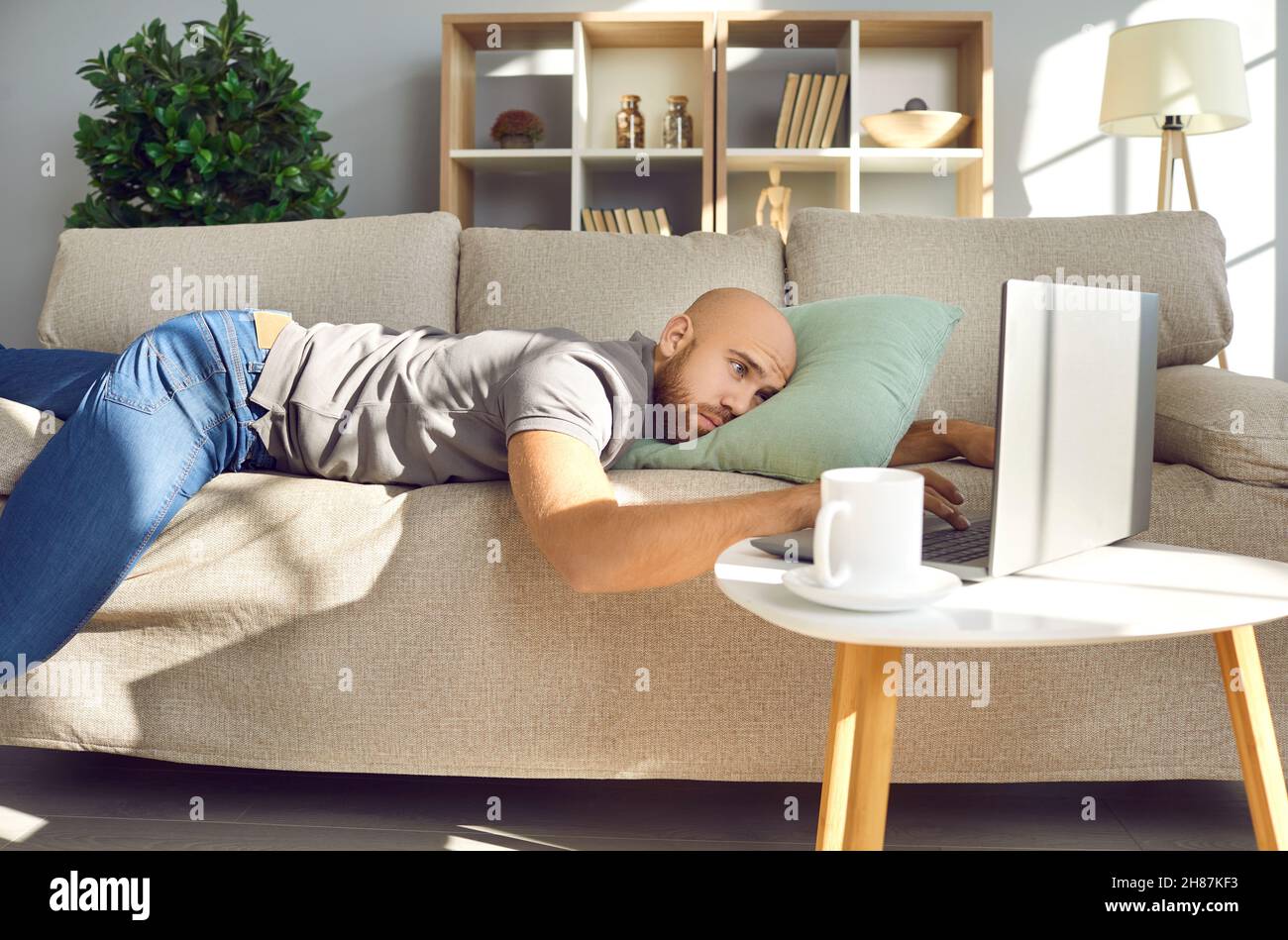 Ennuyé déprimé paresseux jeune homme allongé sur un canapé et regardant son ordinateur portable Banque D'Images