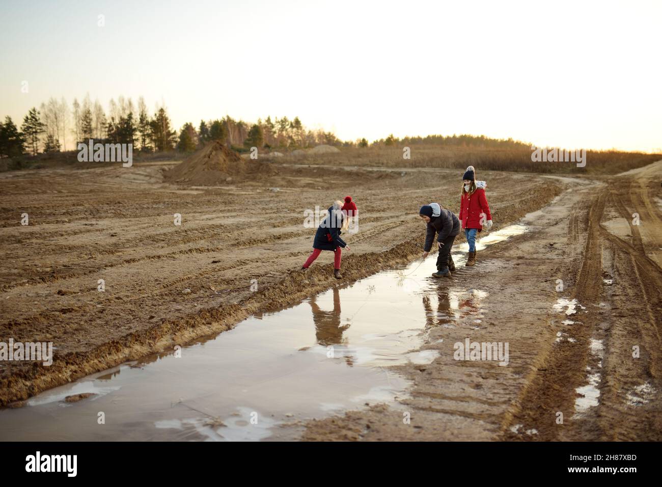 Groupe d'enfants jouant avec de minces flaques de glace formées sur le sol gelé en hiver.Les enfants s'amusent en hiver.Activités d'hiver pour les enfants. Banque D'Images