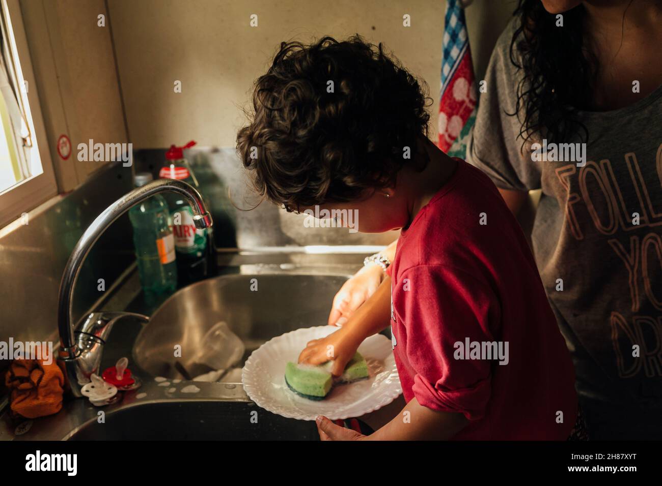 Une petite fille et sa mère lavant des plats ensemble dans la cuisine à la maison. Banque D'Images