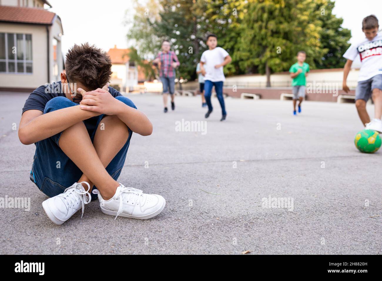 Garçon solitaire assis seul sur le sol, isolé de ses pairs Banque D'Images