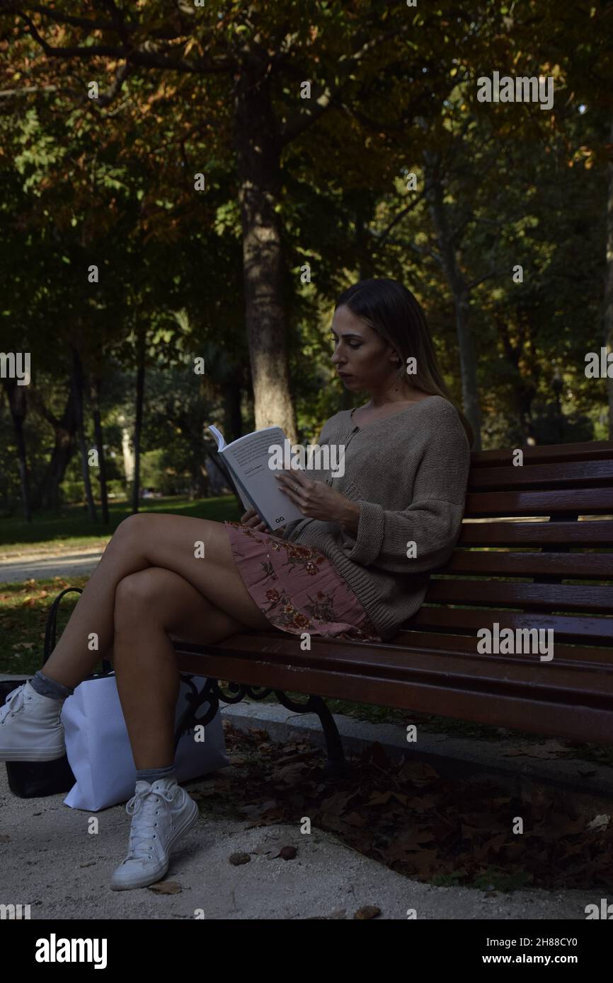 femme lisant un livre dans un parc pendant une journée ensoleillée regardant la caméra, regardant le livre, assis sur un banc, pendant un hiver, jour d'été Banque D'Images