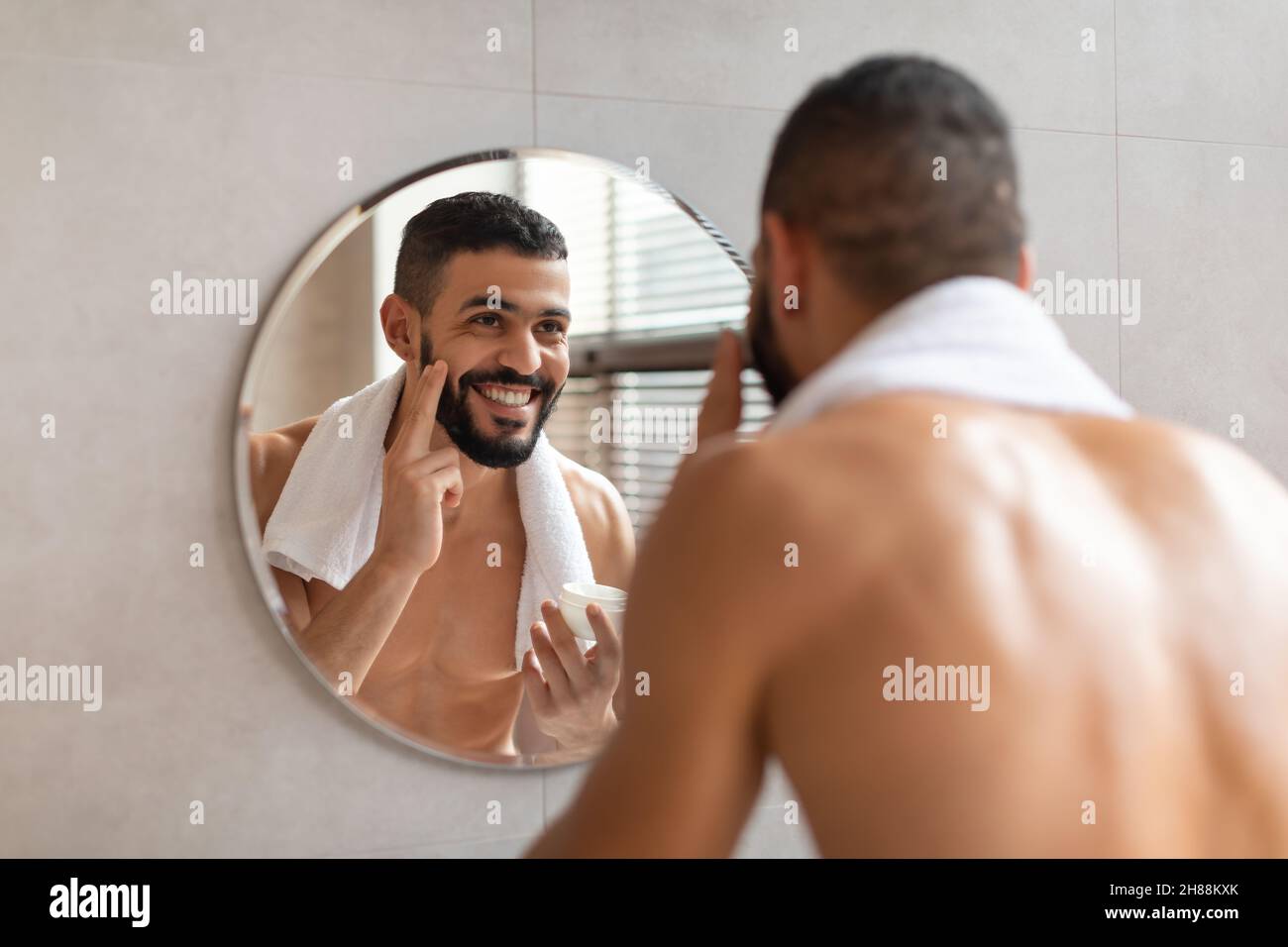 Joyeux gars regardant dans le miroir appliquant de la crème sur le visage Banque D'Images