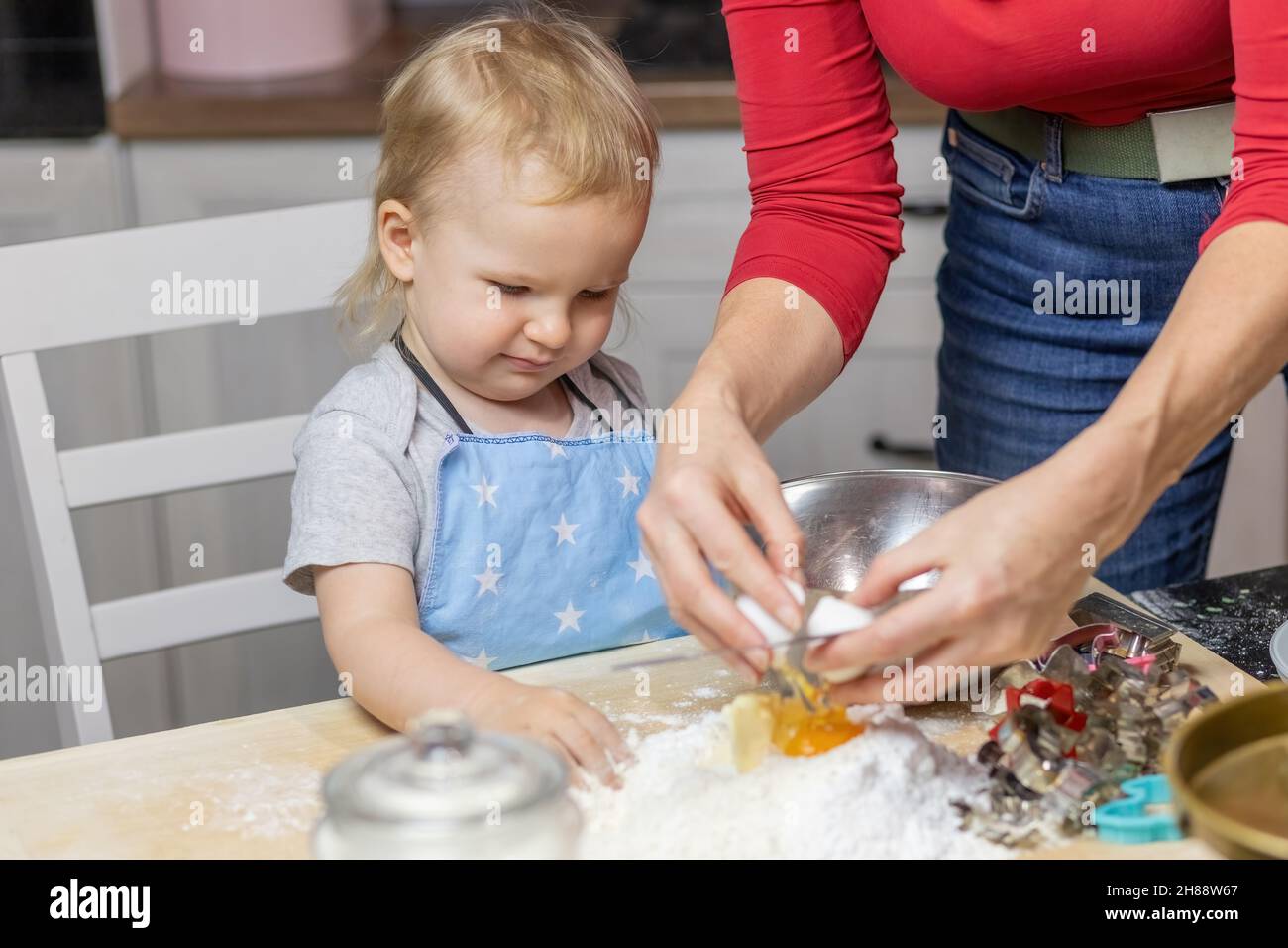 Mignon garçon montres maman met des oeufs dans la farine et prépare la pâte dans la cuisine.Horizontalement. Banque D'Images