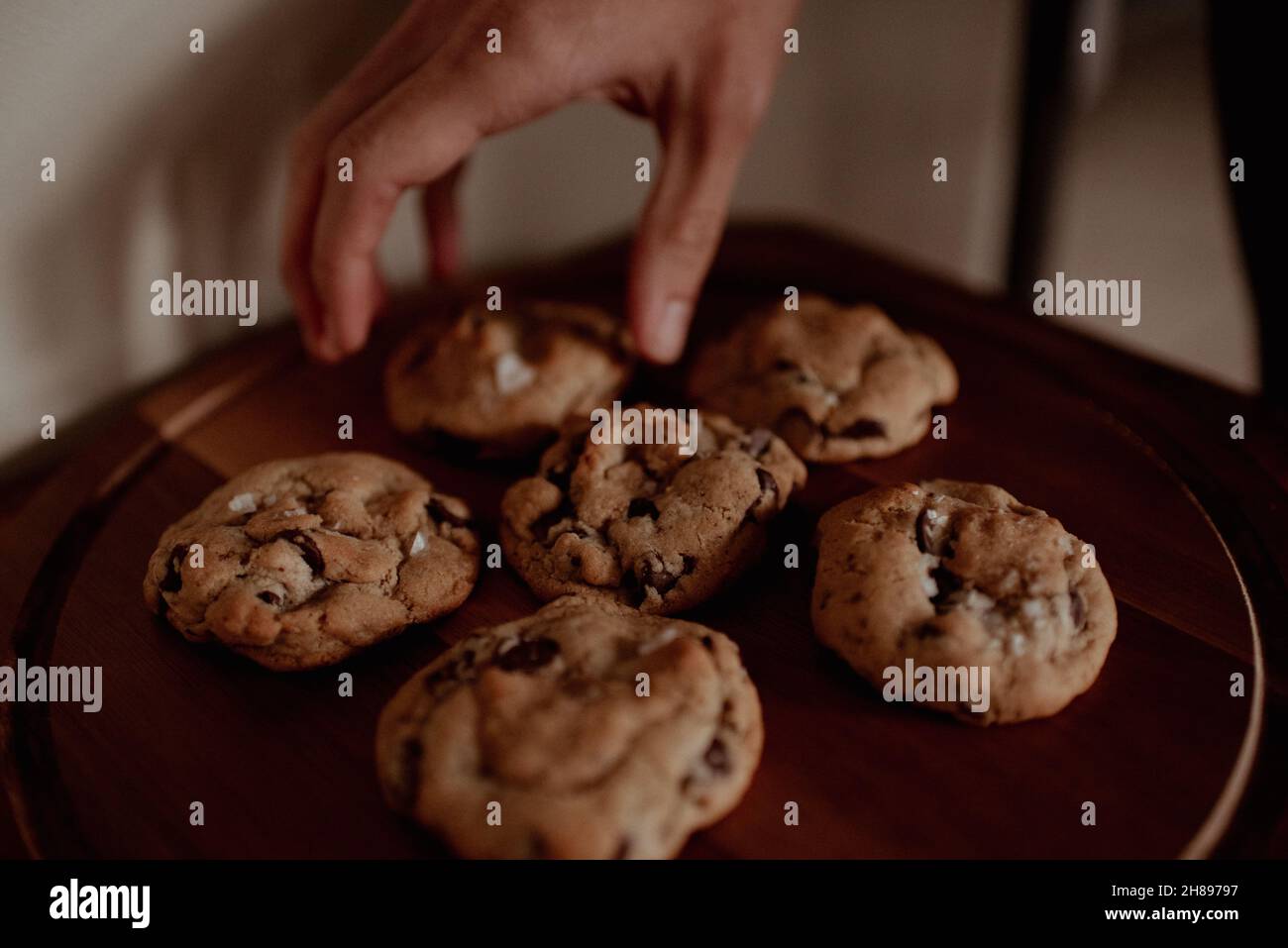 L'homme de course mixte atteint pour des biscuits aux pépites de chocolat salé faits maison.Moody un homme hippster naturellement éclairé atteint pour biscuit et café à la maison ou au café Banque D'Images