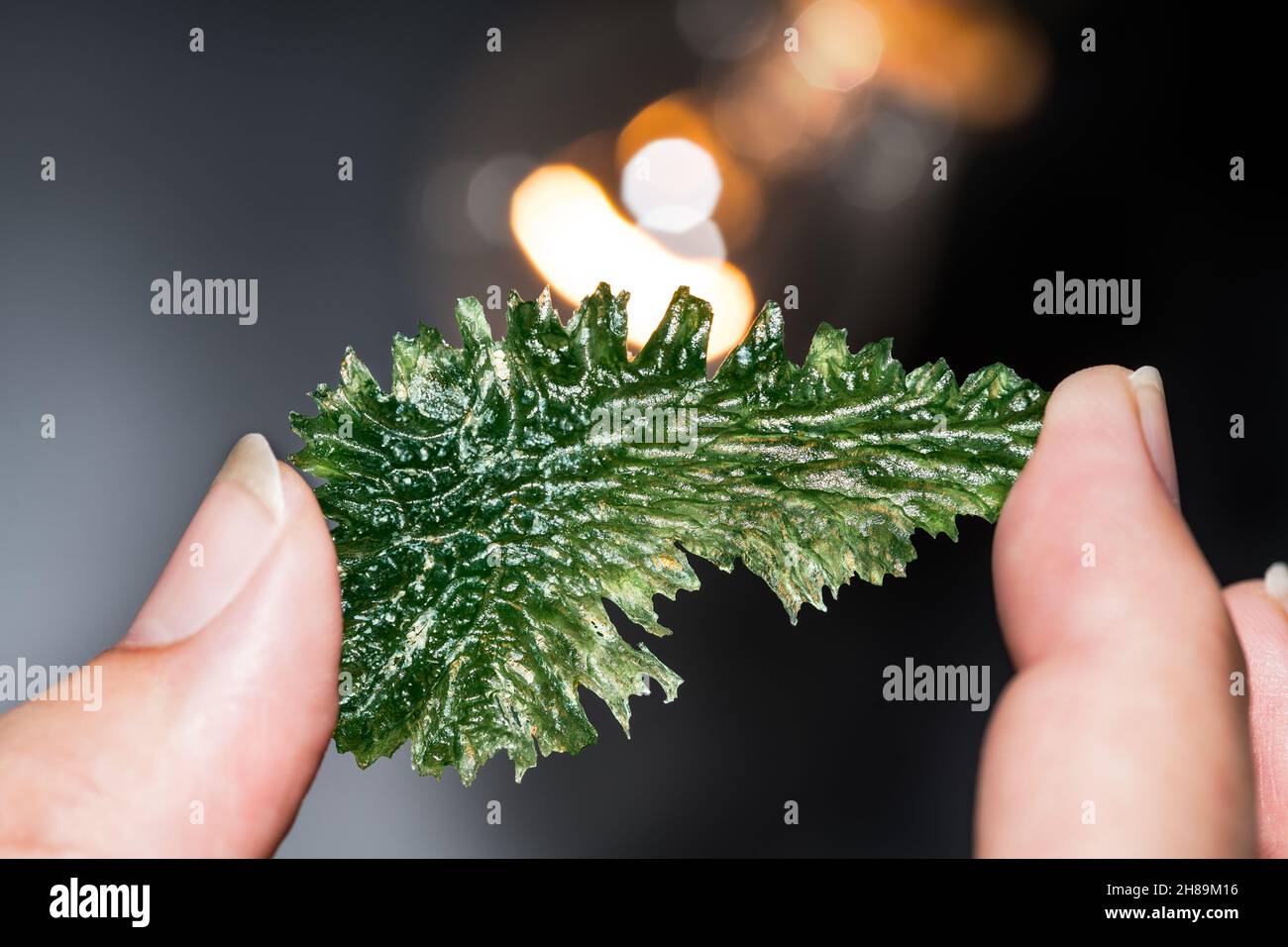 Minéral moldavite vert ridé rare dans la main humaine avec lumière orange et beau bokeh sur fond noir.Collecteur contenant un bijou en verre météorite. Banque D'Images