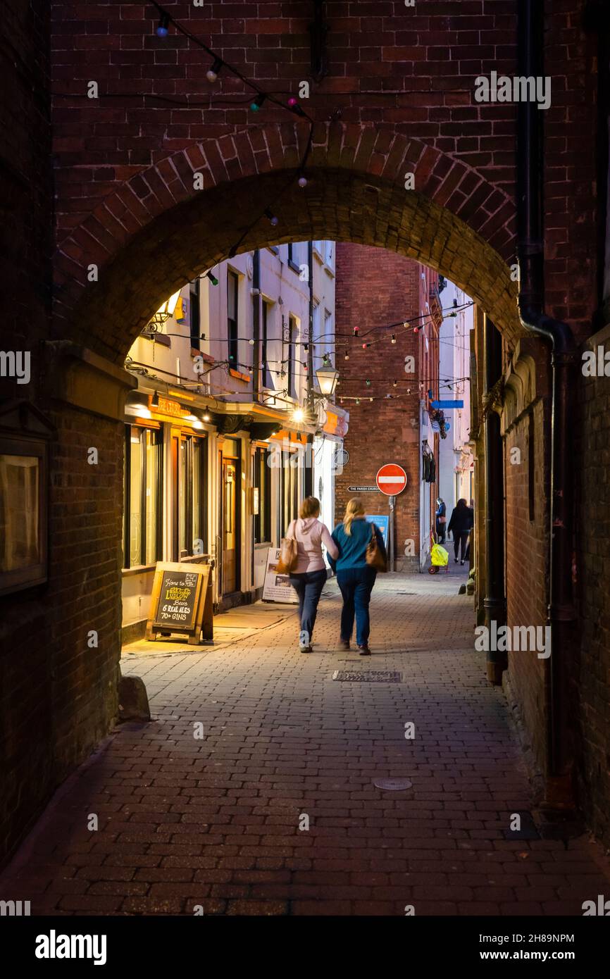 Les gens marchent la nuit à travers une arche en briques sur Church Street, une ruelle étroite qui traverse College Street et King Street. Ludlow, Angleterre Banque D'Images