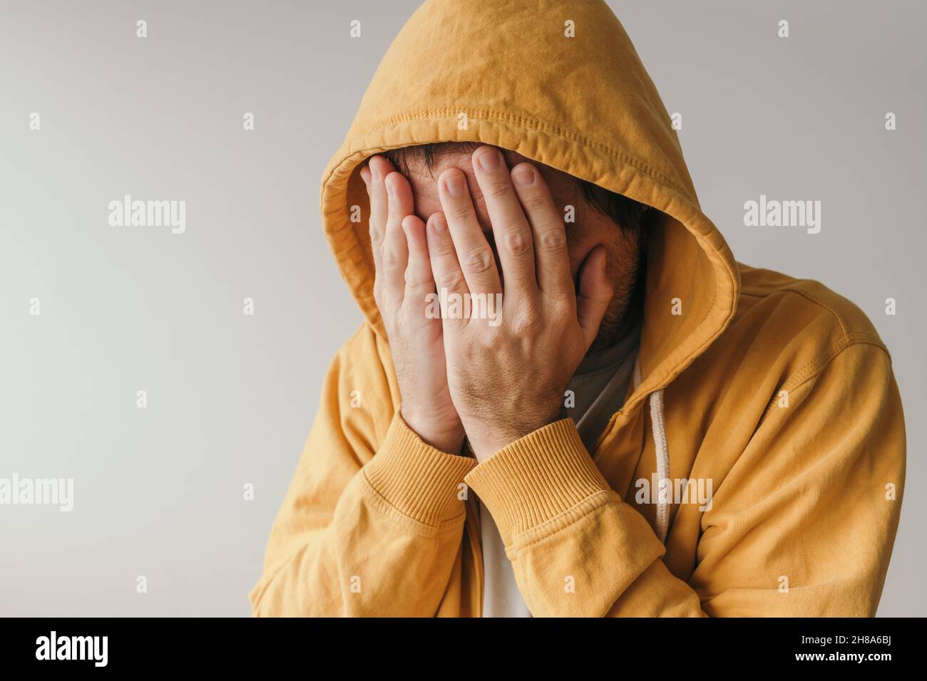 Décontracté triste homme dans le sweat à capuche jaune pleure dans la situation de crise émotionnelle, foyer sélectif Banque D'Images