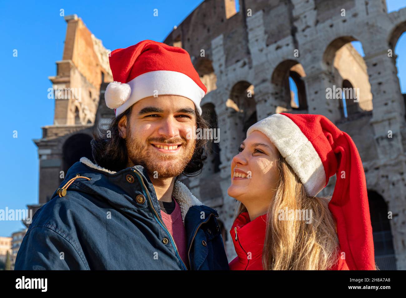 Un jeune couple pose devant le Colisée en chapeaux rouges du Père Noël.Sentiment de bonheur et d'amour.Concept de vacances de Noël. Banque D'Images