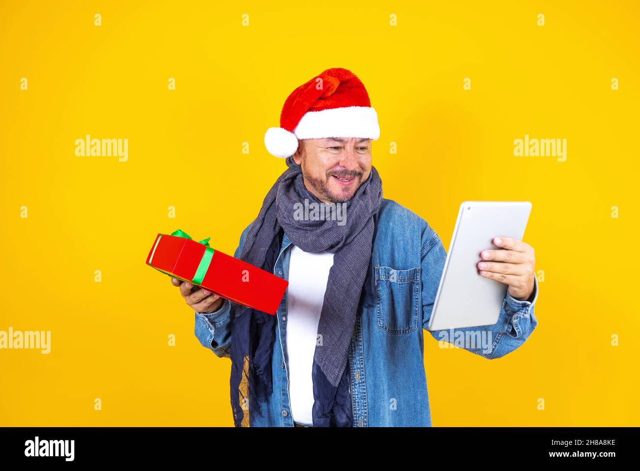 homme latin senior ayant des appels vidéo de noël à l'aide d'une tablette numérique ou d'un pavé tactile sur un fond jaune Banque D'Images homme latin senior ayant des appels vidéo de noël à l'aide d'une tablette numérique ou d'un pavé tactile sur un fond jaune Banque D'Images