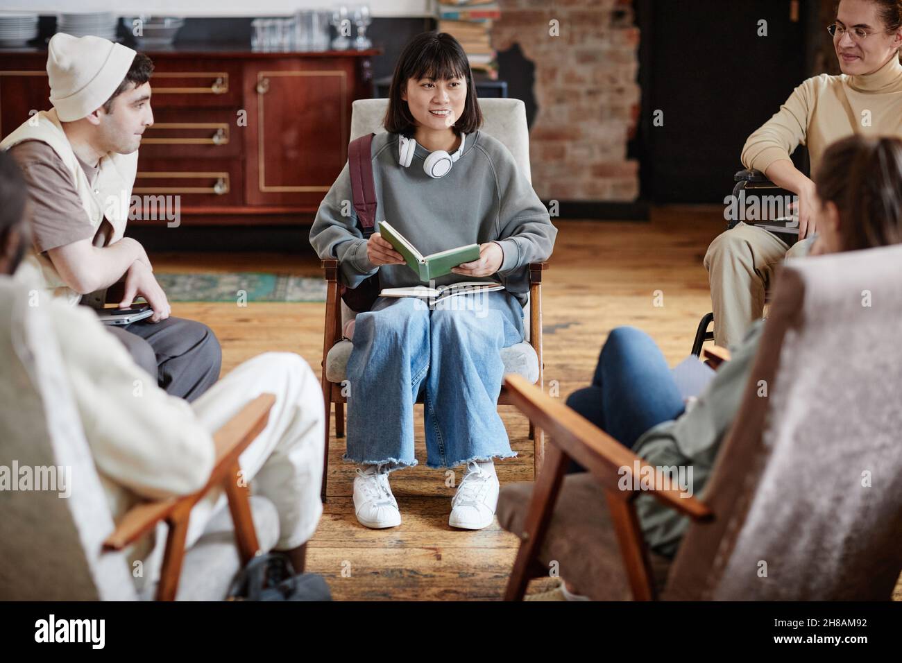 Une jeune femme assise dans un fauteuil et lisant un livre pour un groupe d'élèves pendant les cours Banque D'Images