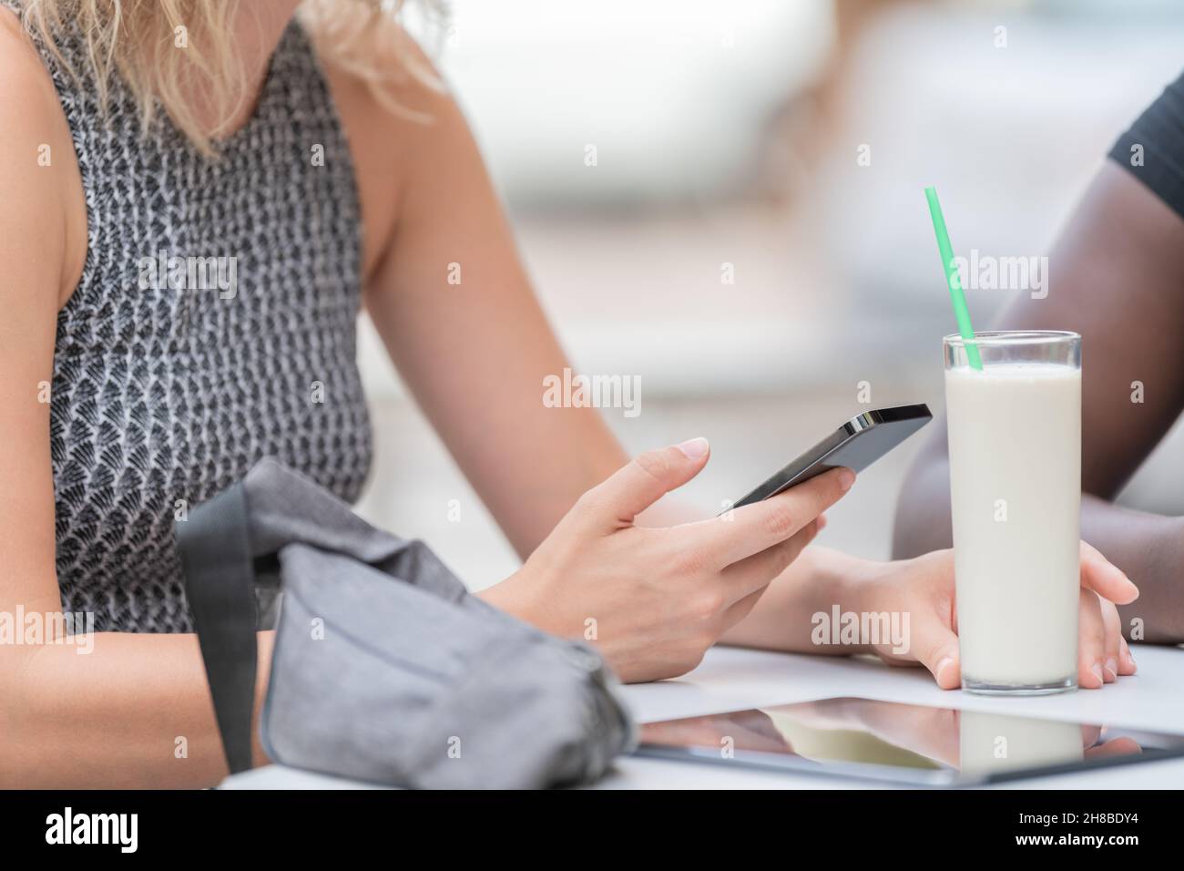 Image rognée d'une personne utilisant son téléphone et tenant un verre de milkshake dans un café extérieur Banque D'Images