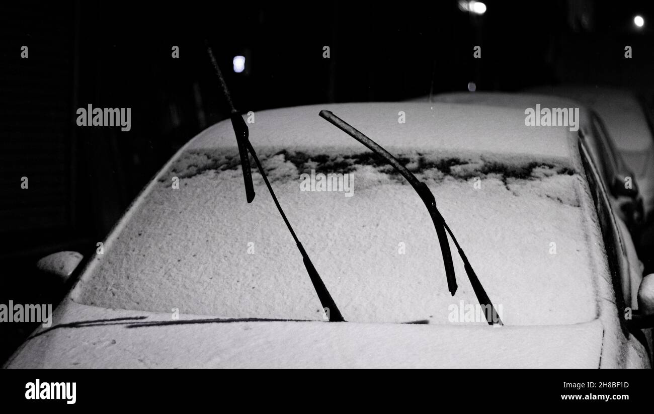 Les essuie-glaces de pare-brise de voiture sont restés en position haute contre le gel dans la neigeVue nocturne des conditions hivernales. Banque D'Images