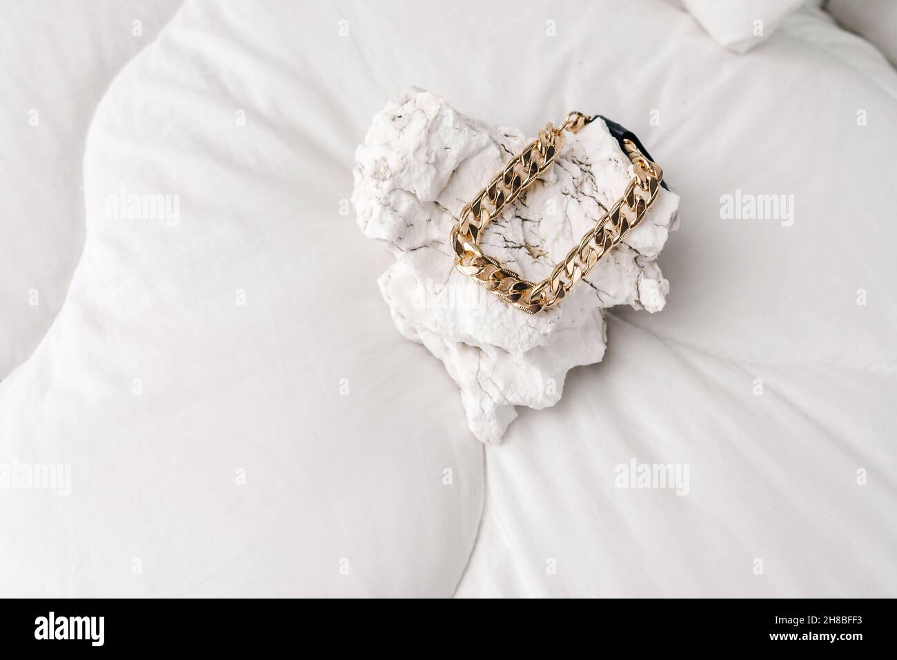 Bijoux fantaisie, bracelet en chaîne de bijouterie dorée sur fond blanc.Pierre blanche comme podium. Banque D'Images