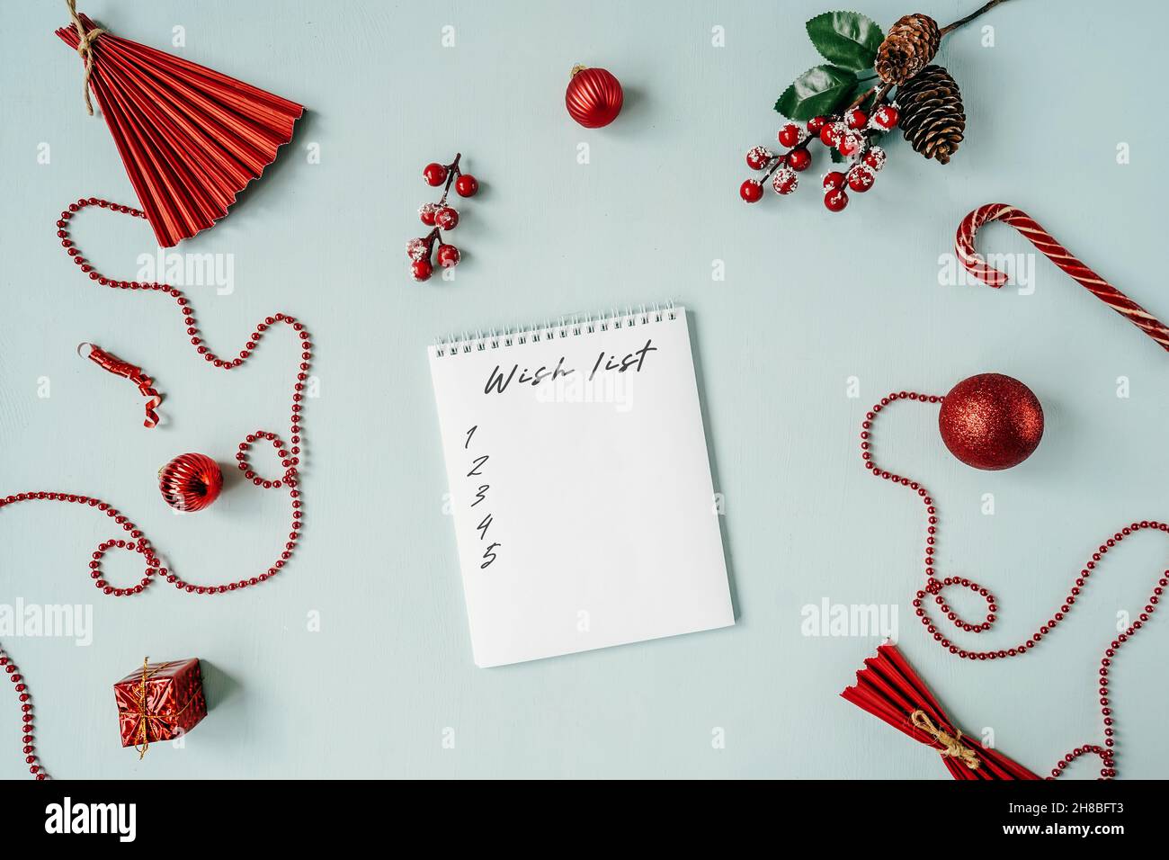 Carnet vierge avec liste de souhaits de texte et rouge boules de Noël décoration autour sur bleu.Pose à plat. Banque D'Images