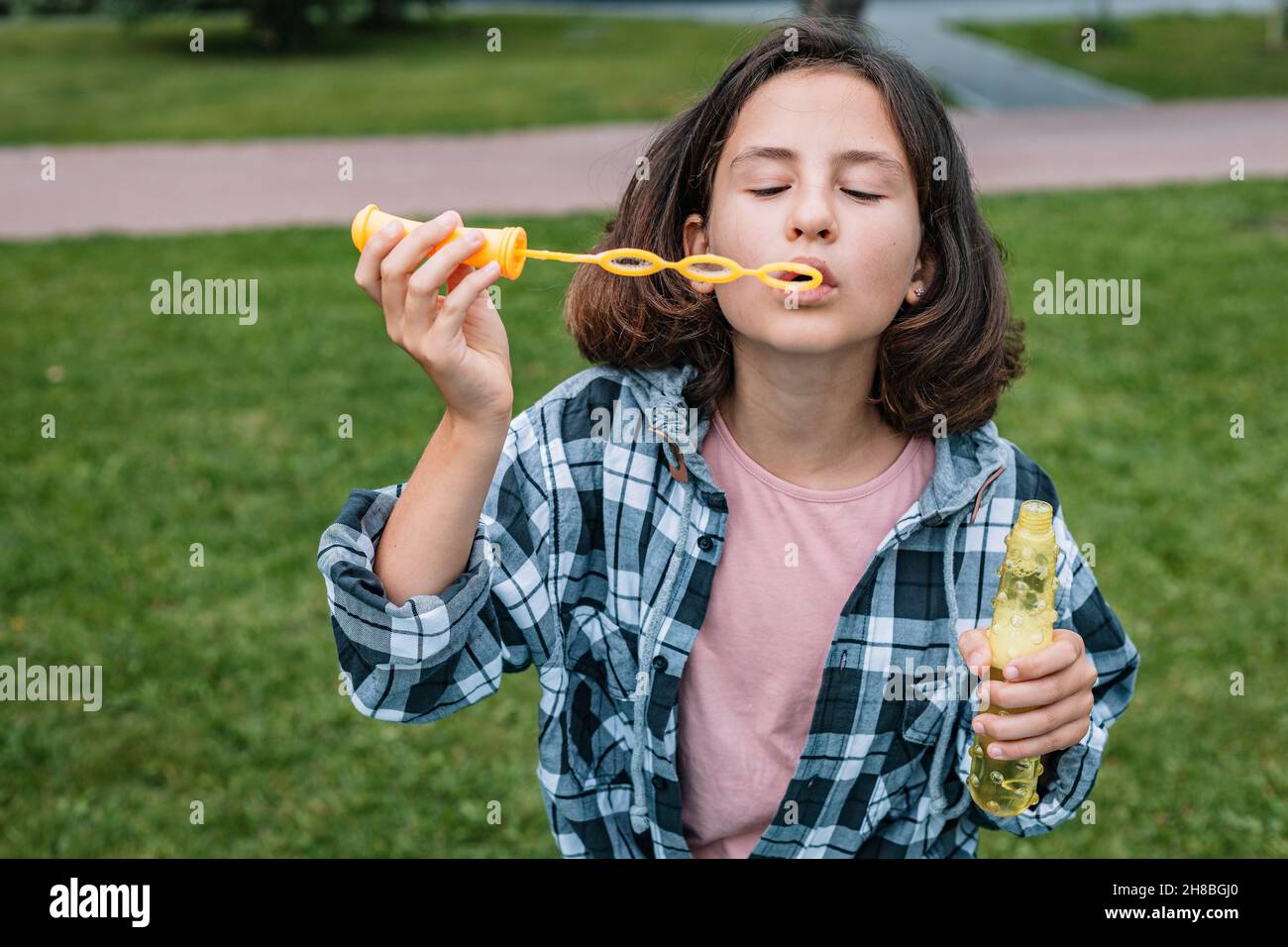 Adorable écolière d'origine caucasienne soufflant de bulles de savon.Portrait d'une belle fille de brunette attrayante ayant du plaisir dans un parc d'été.Em. Positif Banque D'Images