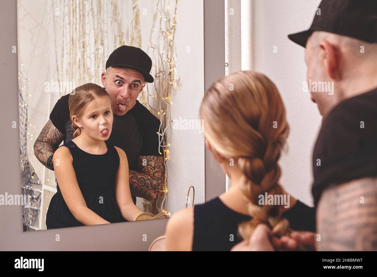 Une petite fille mignonne et son père à embout de tatouage jouent ensemble près d'un miroir.Papa fait les cheveux de sa fille.Vacances en famille et ensemble. Banque D'Images