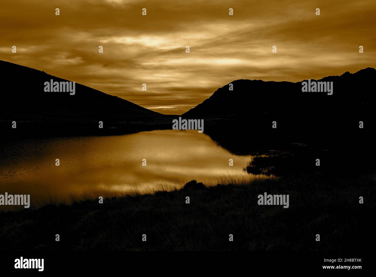 Llyn Pen-y-Gwryd au coucher du soleil, avec des nuages et des montagnes reflétés dans l'eau.Partie du parc national de Snowdonia Banque D'Images