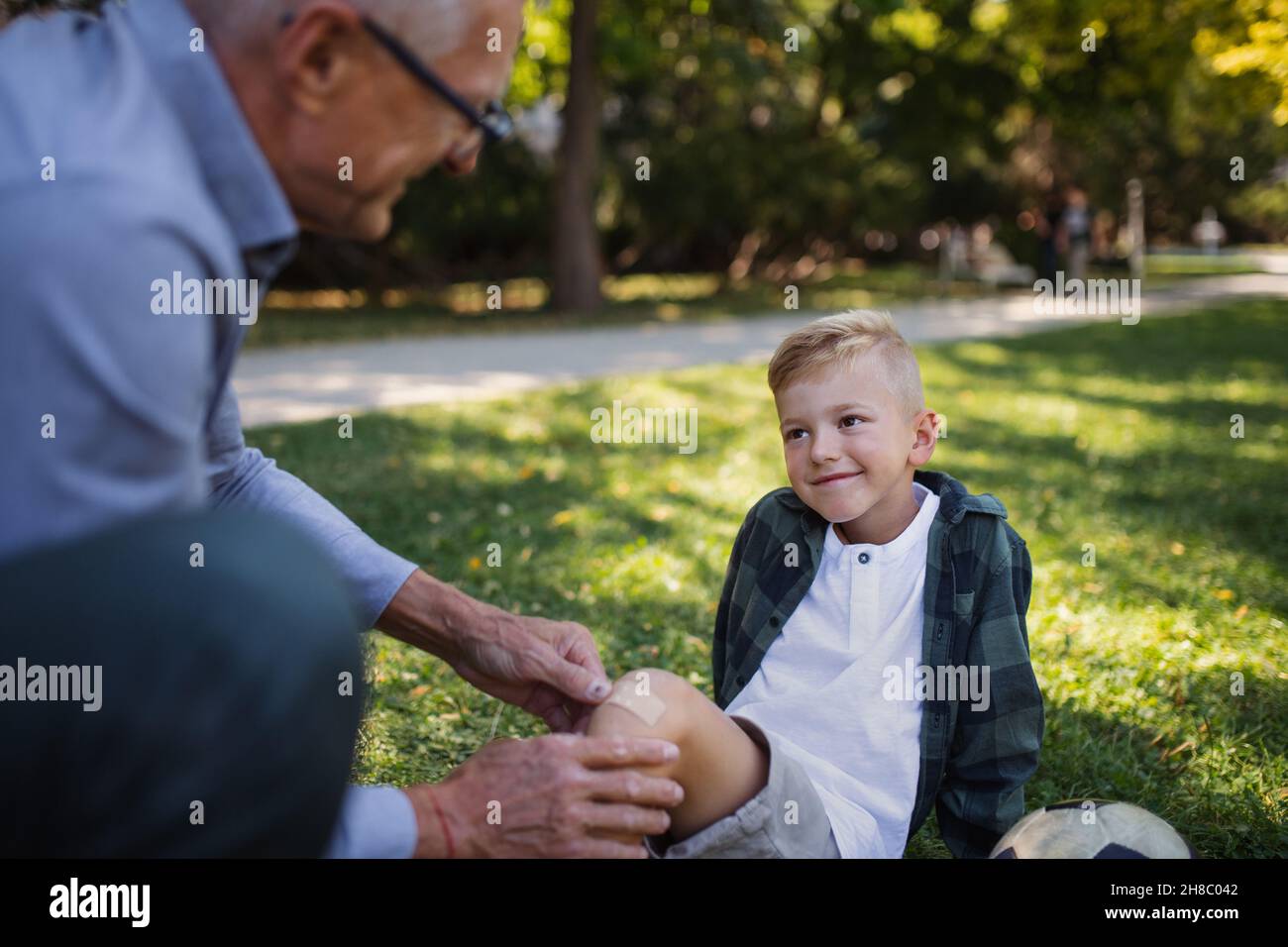 Un petit garçon avec une jambe blessée qui reçoit du plâtre de grand-père à l'extérieur dans le parc. Banque D'Images