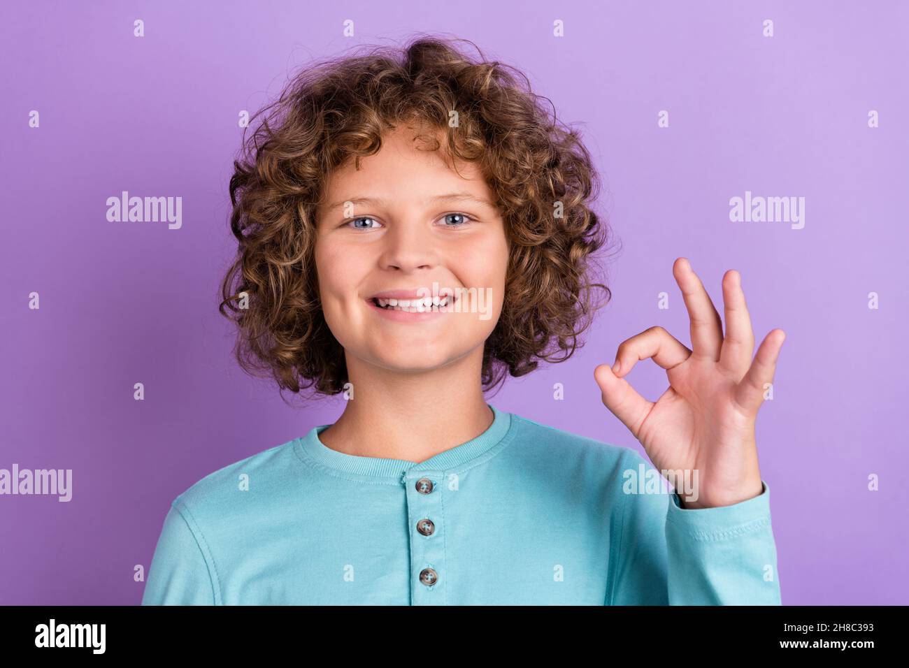 Portrait d'un joli garçon aux cheveux ondulés et joyeux montrant une publicité de signe ok isolée sur fond violet vif de couleur violet Banque D'Images