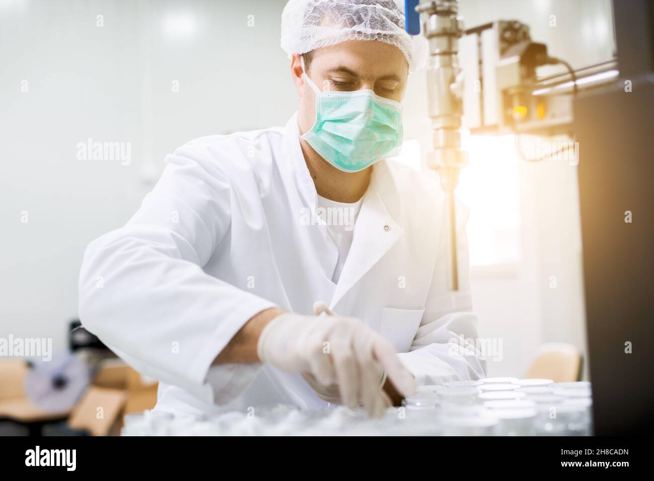 Portrait d'un scientifique masculin en blouse de laboratoire, masque, casquette, réalisant une expérience de travail avec la verrerie Banque D'Images