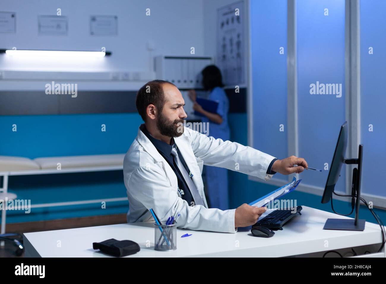 Médecin concentré pointant vers le moniteur pour le travail d'examen pendant le quart de nuit.Médecin regardant l'écran d'ordinateur pour les informations d'analyse et les soins de santé.Spécialiste médical travaillant tard Banque D'Images