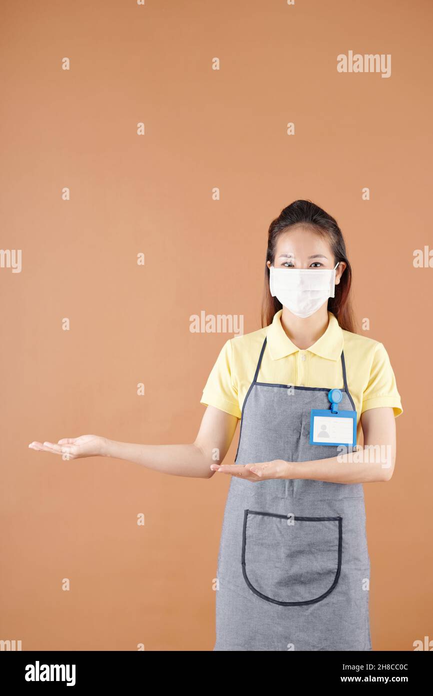 Portrait d'une jolie jeune serveuse montrant un produit invisible, isolé sur le brun Banque D'Images