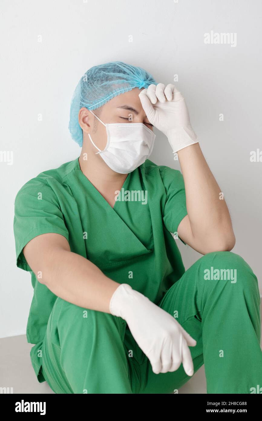 Infirmière masculine stressée et épuisée assise sur le sol dans le couloir de l'hôpital après la chirurgie difficile Banque D'Images