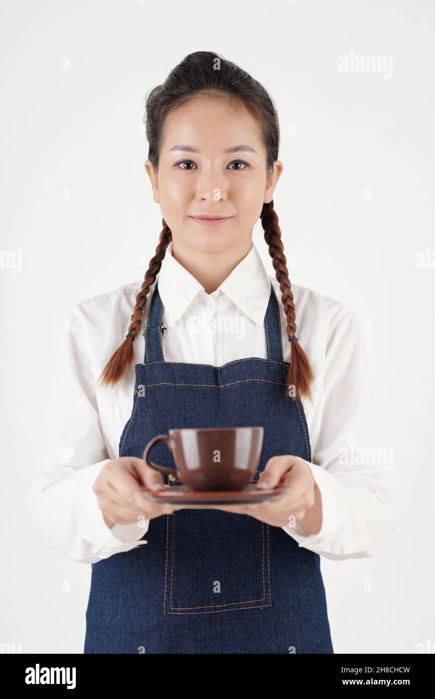Portrait de la jeune serveuse positive servant une tasse de café savoureux au client dans le café Banque D'Images