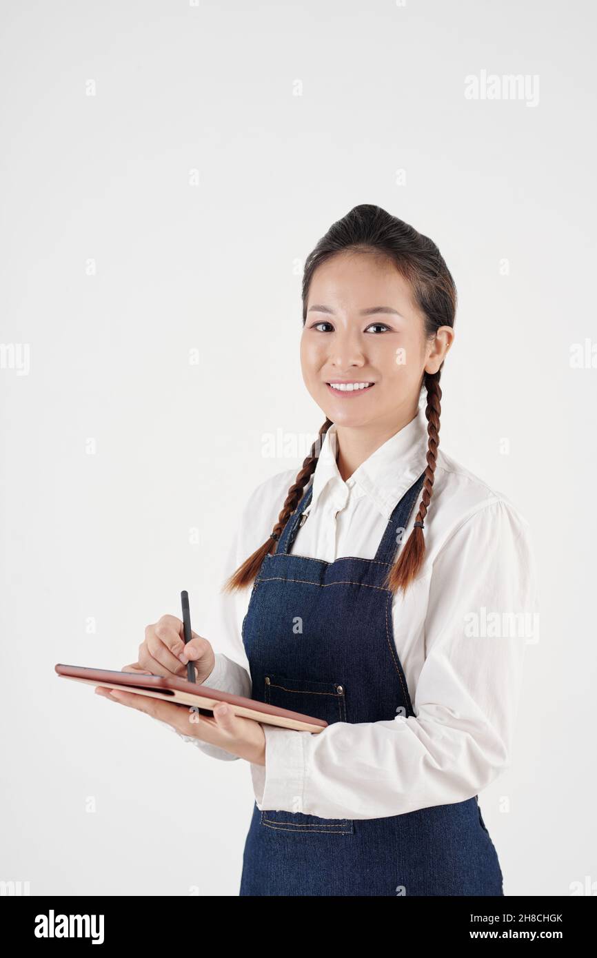 Portrait d'une jeune serveuse souriante acceptant la commande et prenant des notes sur un ordinateur tablette Banque D'Images