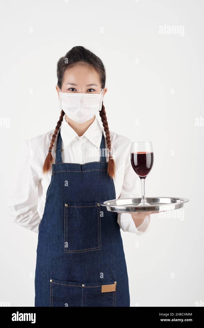 Portrait de la jeune serveuse positive dans un masque de protection avec un verre de vin rouge Banque D'Images