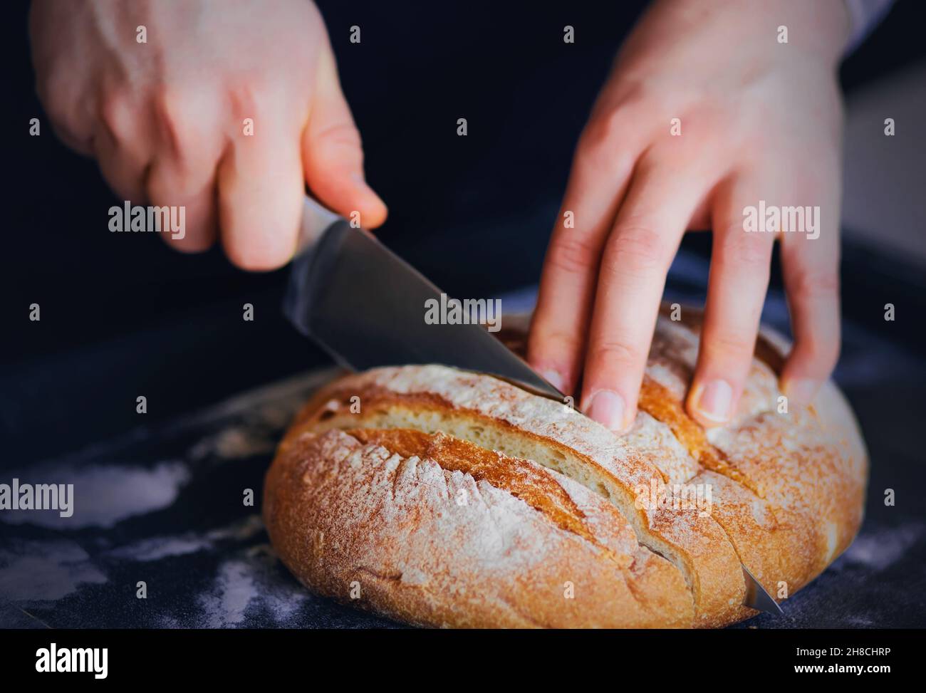 Un homme coupe du pain frais rond de blé avec un couteau tranchant en tranches.Trancher des gâteaux faits maison pour le petit-déjeuner. Banque D'Images