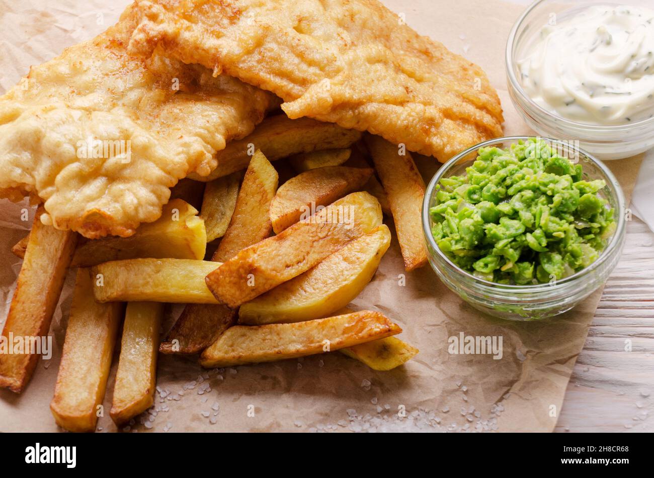 L'alimentation de rue britannique traditionnel fish and chips avec petits pois et sauce tartare sur le papier parchemin Banque D'Images