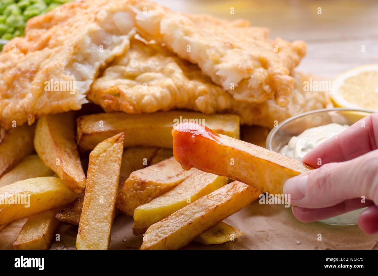 L'alimentation de rue britannique traditionnel poisson et frites avec sauce ketchup et citron sur papier boulangerie Banque D'Images