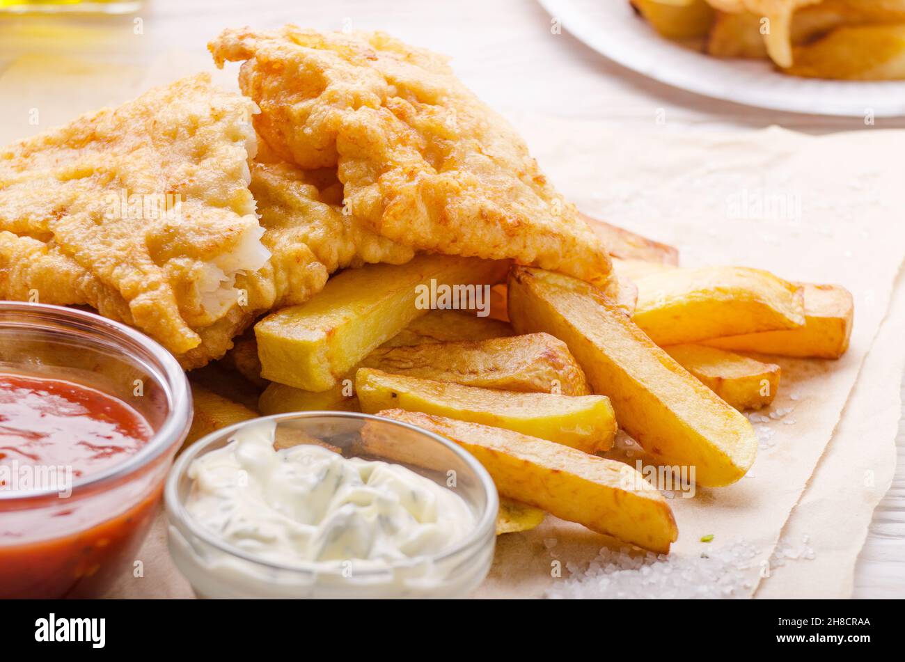 L'alimentation de rue traditionnelle britannique du poisson et des frites avec du ketchup et sauces tartare sur le papier parchemin Banque D'Images