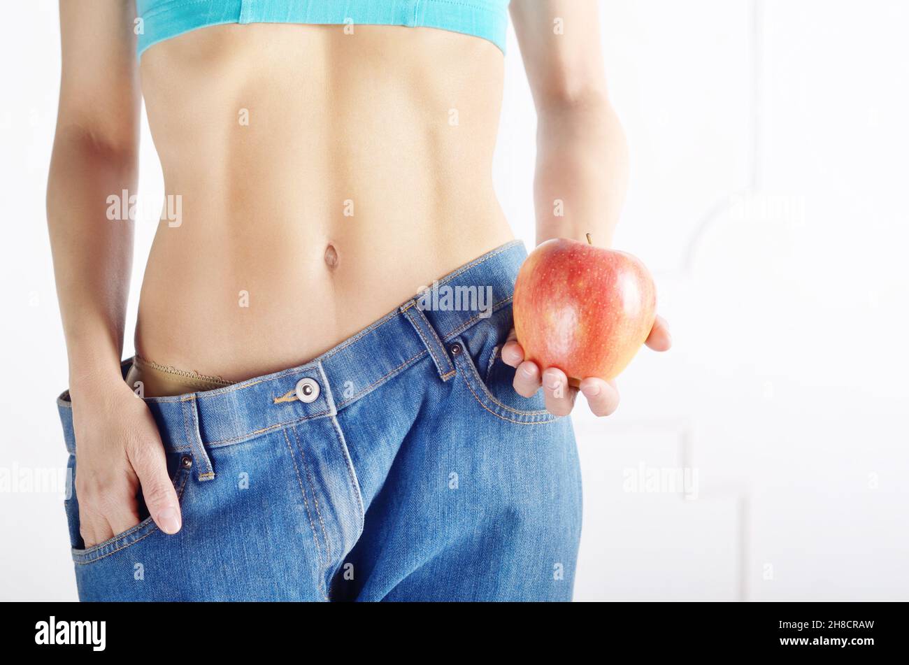 Modèle des femmes de race blanche en bleu jeans avec pomme rouge montrant son ventre plat. Mode de vie sain et concept de Weightloss. Banque D'Images