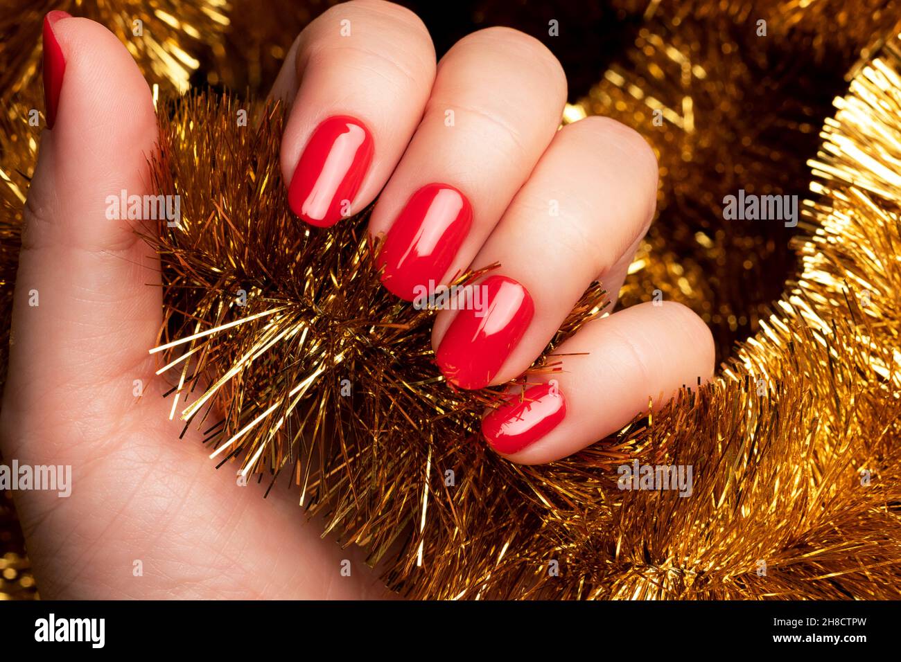 Main féminine avec une belle manucure de vacances - ongles rouges avec fond  doré de Noël tinsel.Concept de soin des ongles Photo Stock - Alamy